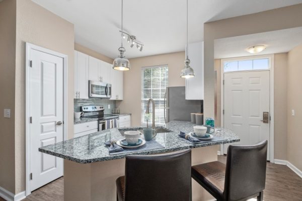 Kitchen with granite countertops, kitchen island with barstools, white cabinetry, and stainless steel appliances, including a built-in microwave, refrigerator, sink,, stove, and oven