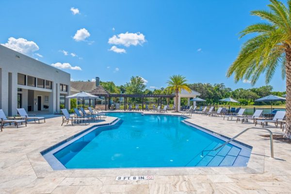 Sparkling, blue pool with surrounding sundeck, ample lounging options, and a view of the clubhouse in the background