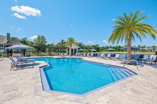 Sparkling, blue pool with surrounding sundeck, ample lounging options, and a view of the lake in the background