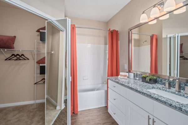 Bathroom with long, single vanity sink with granite countertops, ample storage, a large mirror, shower bath, and a walk-in closet