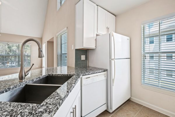 Closeup of kitchen island, granite countertops, dishwasher, sink, refrigerator, and white cabinets.