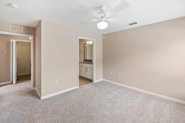 Unfurnished, carpeted bedroom with ceiling fan and entrance to connected bathroom